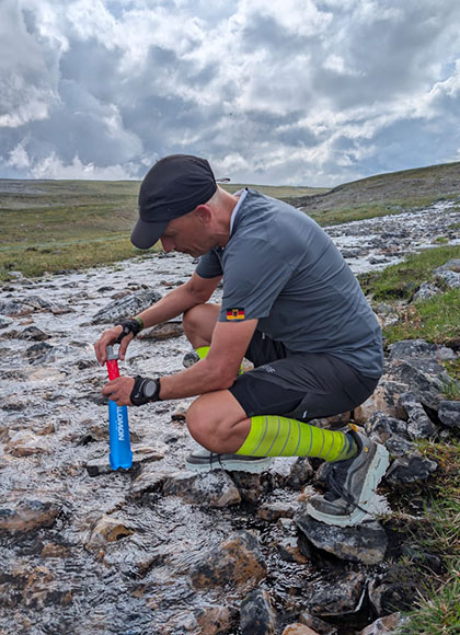 Ingo füllt im Bach die Wasserflasche